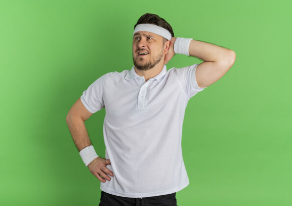 站身穿白衬衫 头戴头巾 手放在头上 困惑地站在绿色背景下的年轻健身男子绿色看男士