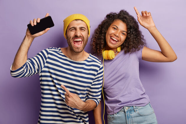 积极快乐的混血青年男女尽情跳舞 通过手机应用听音乐 戴耳机 穿着休闲服沟通娱乐乐趣