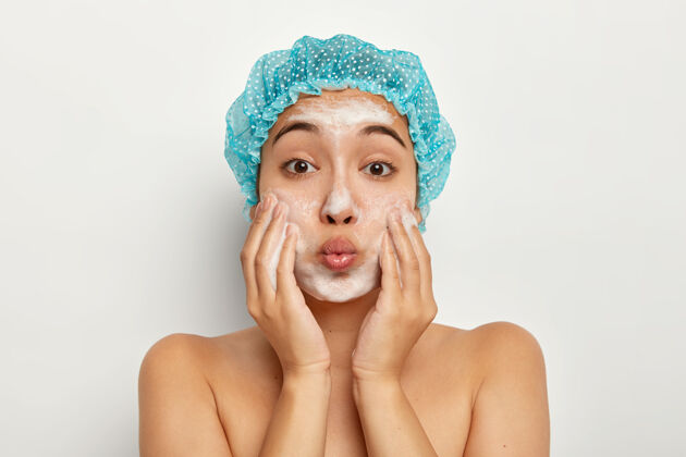 赤膊双唇合拢的可爱女性特写肖像 在脸上涂上肥皂 洗干净皮肤 裸体站立 呵护脸部卫生淋浴健康
