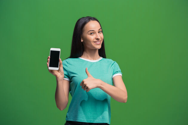 广告一个微笑的女人在绿色背景下展示一个空白的智能手机屏幕空白电话手