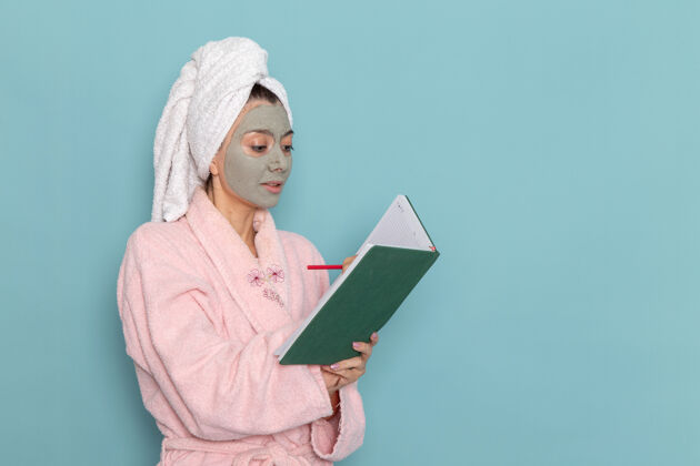 浴室正面图年轻女性穿着粉色浴袍淋浴后在蓝色墙上写着美容水霜自护淋浴浴室人自我照顾年轻
