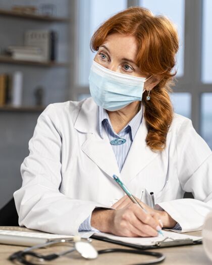 医生女医生戴着医用口罩在办公桌前写处方的正面图全科医生处方工作