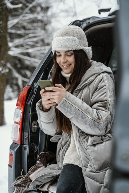 户外微笑的女人在路上用智能手机开车旅居雪自然