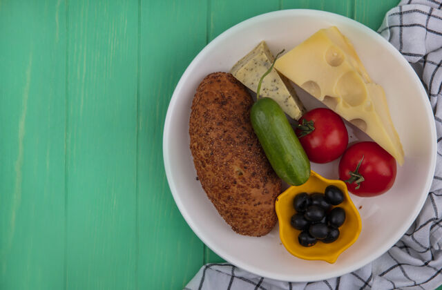 奶酪白色盘子上美味的芝麻馅饼的俯视图 绿色木制背景上有新鲜蔬菜 奶酪和橄榄 还有复印空间盘子蔬菜绿色