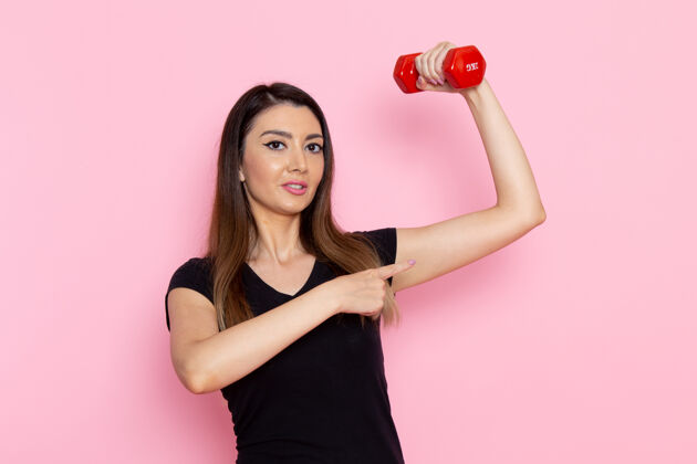 举行正面图年轻女性手持哑铃在浅粉色墙上运动员运动锻炼健康锻炼视图模特成人