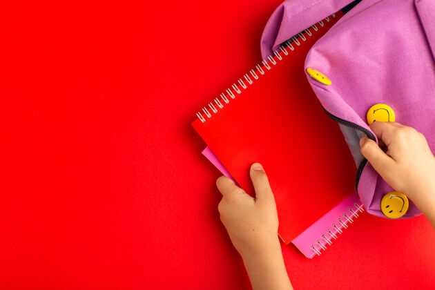 采取俯视图：准备上学的小孩从红色表面的袋子里拿文案准备小照顾