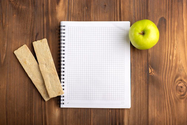 记事本俯视图打开蓝色的复写本与饼干和绿色的苹果在棕色的书桌上史密斯奶奶板健康