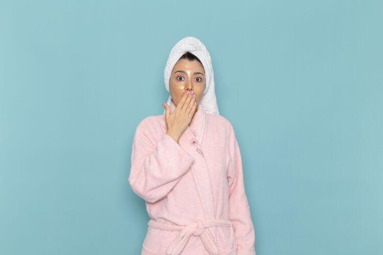 自我护理正面图年轻女性穿着粉色浴袍淋浴后捂着嘴在浅蓝色的墙上美容水自理淋浴干净清洁封面视图