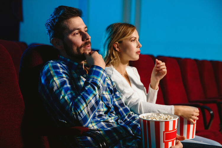 室内迷人的年轻白种人夫妇在电影院 房子或电影院看电影看起来富于表现力 惊讶和情绪化独自坐着玩关系 爱情 家庭 周末时间成人女孩微笑