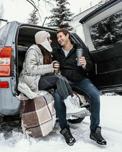 女人低角度的幸福夫妻在汽车的后备箱里喝热饮 而在公路旅行汽车航行冒险