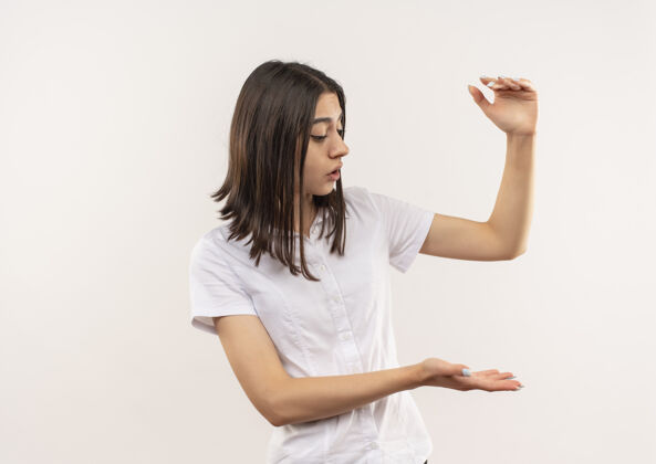 女人穿白衬衫的年轻女孩一边看一边用手做着展示身材的手势 一边站在白墙上测量标志测量站公民