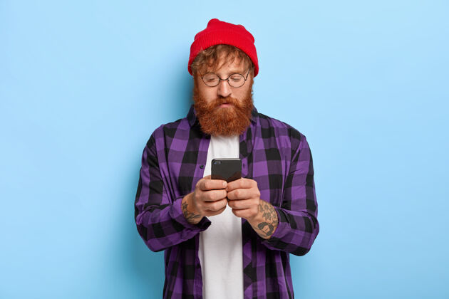 通知红发浓密胡须的时尚潮人 专注于智能手机 收到一些出版物的链接眼镜姜电话
