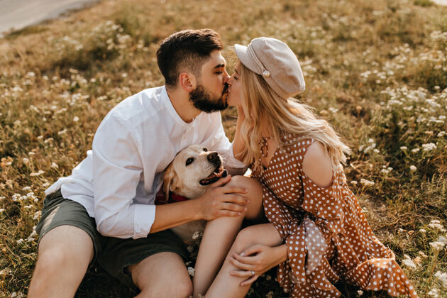 户外男人和女人在公园里接吻这对夫妇和他们的拉布拉多犬坐在草地上享受美好的一天关系家庭夫妇