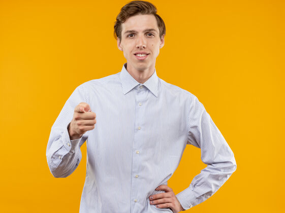 男人身穿白衬衫的年轻人用食指指着橙色的墙上自信地站着微笑自信年轻橘子