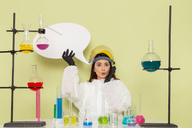 化学正面图身着特殊防护服的年轻女化学家手持绿色墙上的白色标牌工作化学实验室化学女科学特殊保护科学
