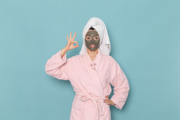 实验服正面图：年轻女性 穿着粉色浴袍 淋浴后带面罩 蓝色墙面 美容水霜 自我护理淋浴浴室浴袍后面浴室
