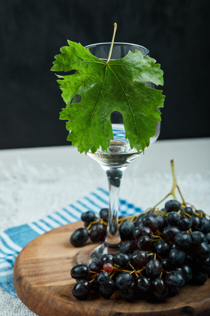 美味一束黑葡萄和一杯白桌子上有叶子的葡萄酒盘子玻璃食物
