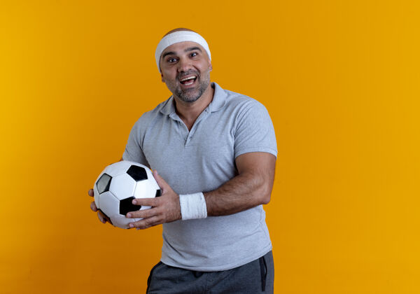 人成熟的运动型男人戴着头巾 拿着足球 面带微笑 站在橙色的墙2上 望着前方足球运动站着