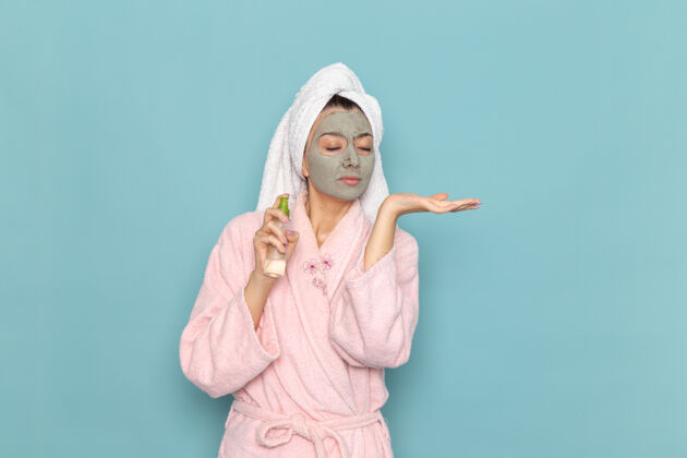 后面正面图：年轻女性穿着粉色浴袍 淋浴后在浅蓝色墙面上使用喷雾美容洁面水自理淋浴清洁长袍服装