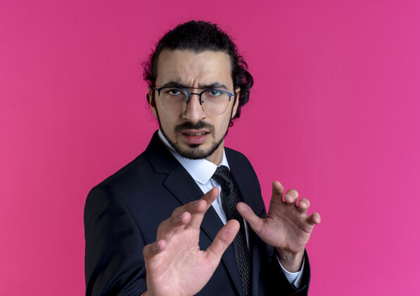 制造一个穿着黑西装戴着眼镜的商人站在粉红色的墙上用厌恶的表情做着防御的手势西装生意优雅