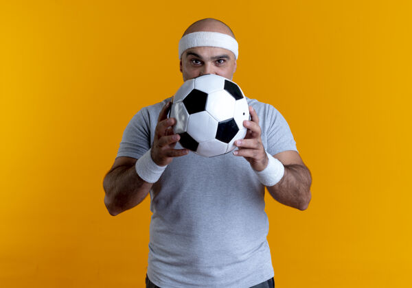 足球成熟的运动型男人戴着头巾 手里拿着足球 站在橙色的墙上望着前方运动运动装运动
