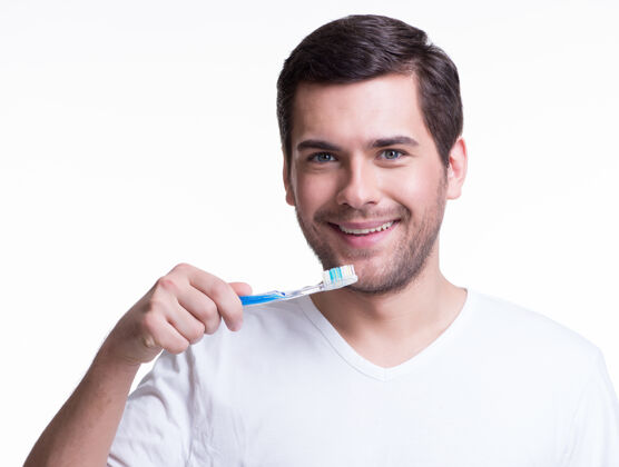 年轻人一个微笑的年轻人 穿着白色t恤 手里拿着牙刷牙刷帅哥成人