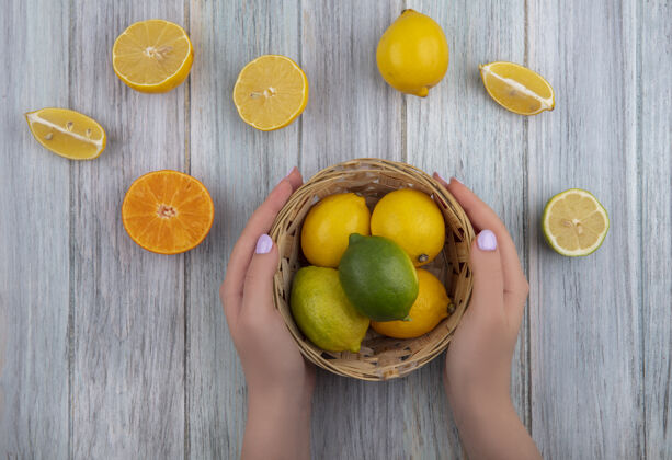 顶部俯视图：女人拿着篮子里的柠檬和灰色背景上的橘子片食物橙子柑橘