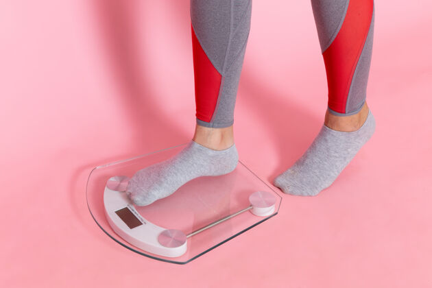 运动正面图：年轻女性在粉色墙壁上测量体重运动锻炼运动员腰部美丽脚女性重量