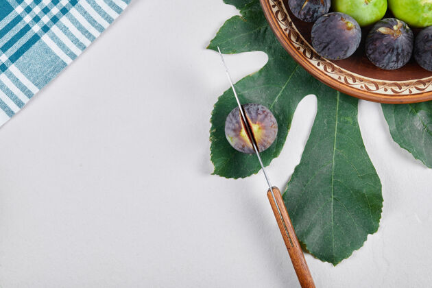 陶瓷绿色和黑色无花果在一个陶瓷板与刀和叶无花果食物水果