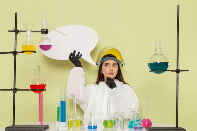 实验室外套正面图身着特殊防护服的年轻女化学家手举白色大牌子在绿色墙上化学工作女科学实验室实验室前面年轻