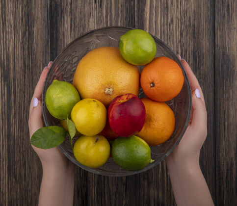 持有顶视图女人拿着一个水果花瓶 柚子 橘子 酸橙 李子 桃子 背景是木制的花瓶食物水果