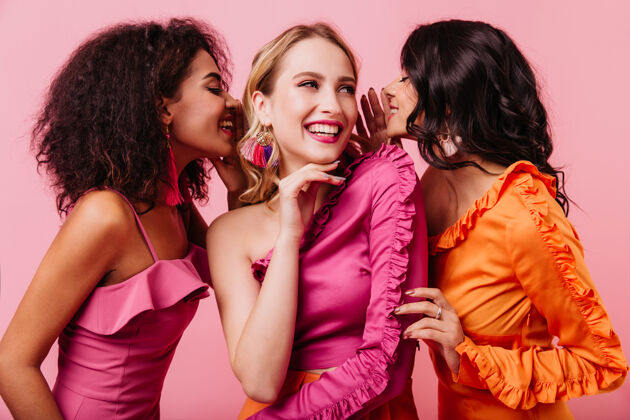 情感三位国际友人在粉红色墙上微笑的工作室肖像谣言听到八卦
