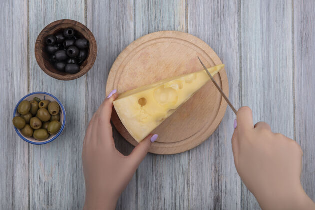 观点俯视图：一位女士在架子上切马斯坦奶酪 灰色背景上有黑色和绿色的橄榄绿色马斯丹奶酪