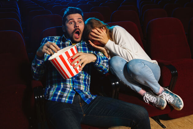 大厅迷人的年轻白种人夫妇在电影院 房子或电影院看电影看起来富于表现力 惊讶和情绪化独自坐着玩关系 爱情 家庭 周末时间观众微笑电影