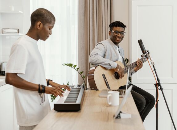 水平侧视图男音乐家在家里弹吉他和电子键盘表演人才乐器手