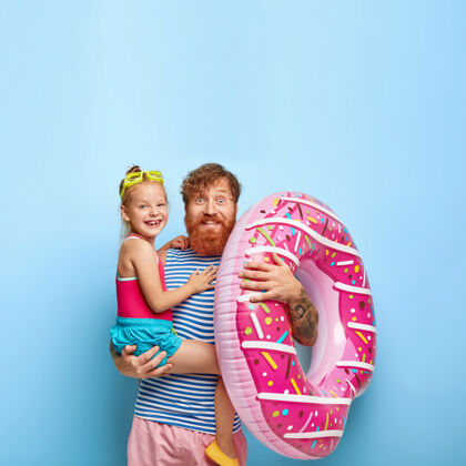 条纹快乐的红发家庭在海岸线玩得很开心快乐的胡须爸爸抱着小女孩和充气的游泳圈父母在一起享受