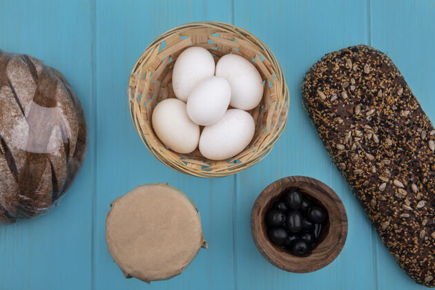 吃顶视图黑色橄榄在一个碗里 鸡蛋在篮子里 黑面包在绿松石背景上食物篮子顶部