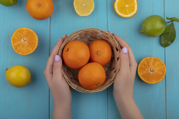 酸橙俯瞰图：一位女士在蓝绿色背景上用柠檬和酸橙在篮子里切橘子柠檬绿松石水果