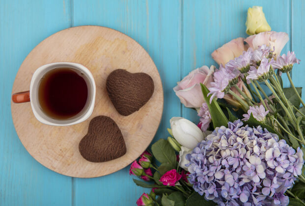 饼干茶杯和心形饼干的俯视图放在切割板上 蓝色背景上有花朵顶部板心形