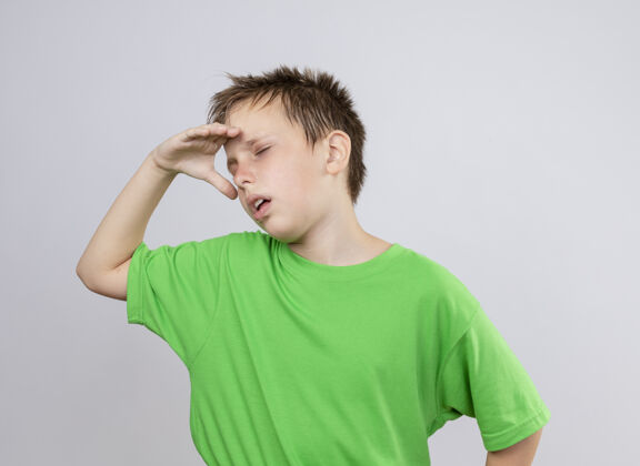感情生病的小男孩穿着绿色t恤 站在白色的墙上感觉不舒服 因为寒冷男孩不适小