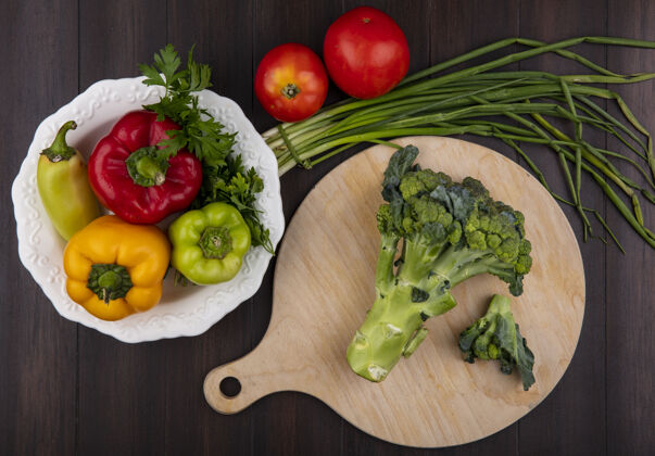 蔬菜在砧板上俯瞰西兰花 盘上放着甜椒 木制背景上放着洋葱和西红柿洋葱食物绿色