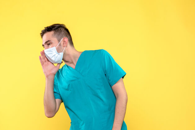人黄色墙上戴着无菌口罩的男医生的正视图男性医生脸胡子