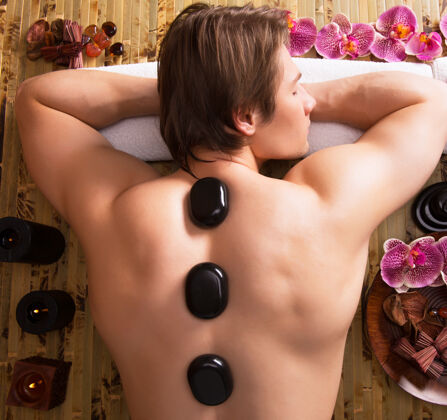 男人帅哥在spa沙龙做石头按摩 健康的生活方式兰花金发治疗