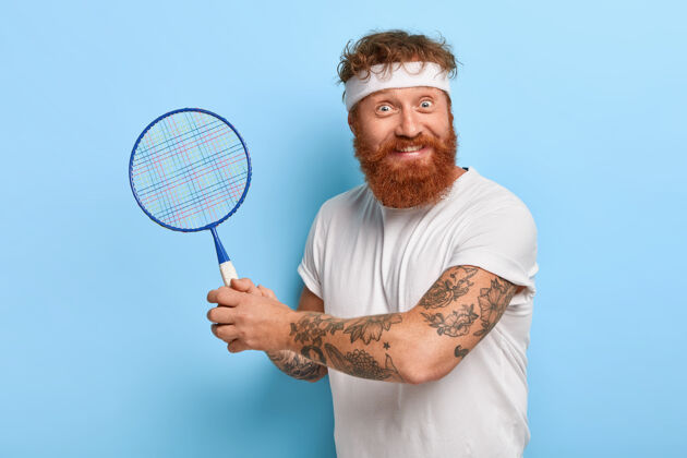 球拍高兴的运动员拿着网球拍 戴着白色的头带 t恤活跃小伙子羽毛球