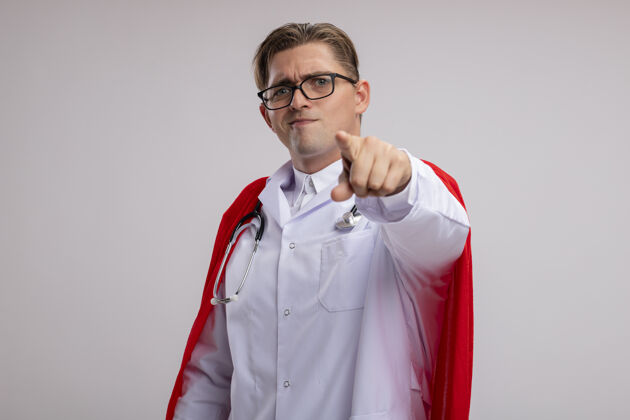 目录超级英雄医生身穿白色外套 披着红色斗篷 戴着眼镜 脖子上戴着听诊器 食指微笑着站在白墙上听诊器眼镜男人