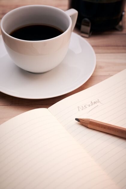桌子一个文本“星期一”写在笔记本上的一个白色咖啡杯的侧面垂直拍摄咖啡写作铅笔