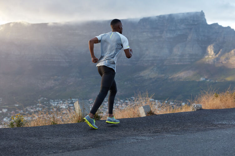 紧身裤活跃的黑皮肤男人在行动中的背照 穿越山路 过着健康的生活方式 有耐力和动力去健身 在山上摆姿势 享受大自然天空乡村教练