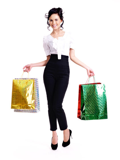 包幸福女人的全画像 带着彩色购物袋 孤立地站在白色的墙上购物购物者成人