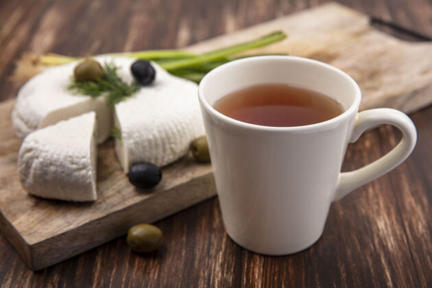 羊奶侧视图：一杯茶 放在木制背景的架子上 上面放着菲塔奶酪 橄榄和葱早晨绿茶茶