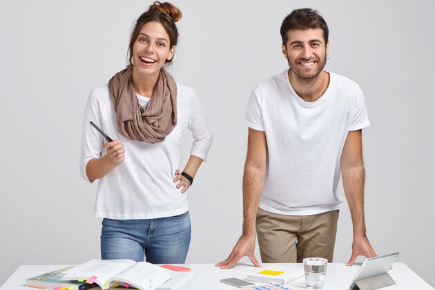 专家身着时尚服装 站在白色书桌旁 研究文学 在平板电脑上制作项目 连接无线互联网的快乐男女设计师的照片团队合作高兴小玩意